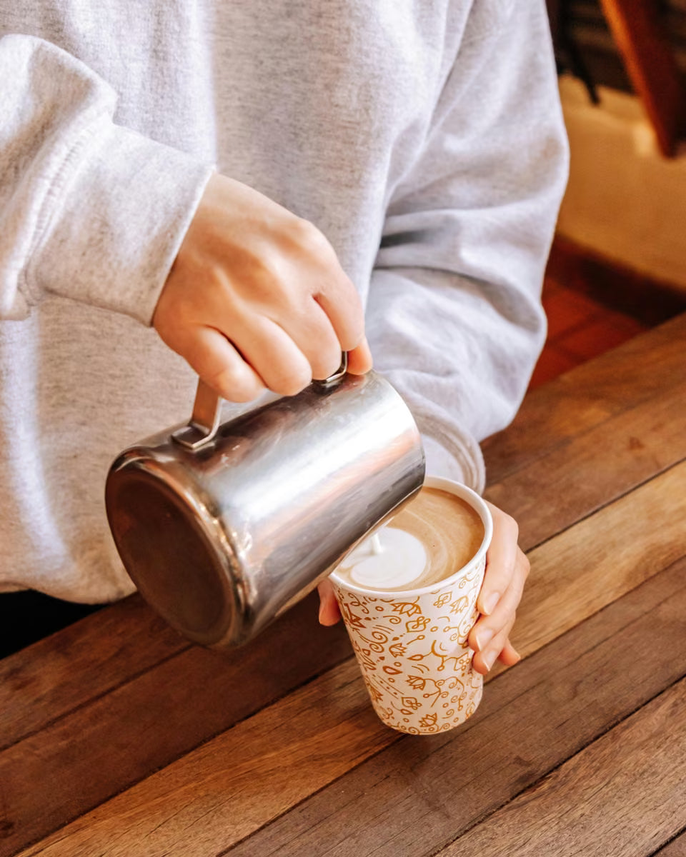 A barista pouring milk into a Hidden Grounds cup